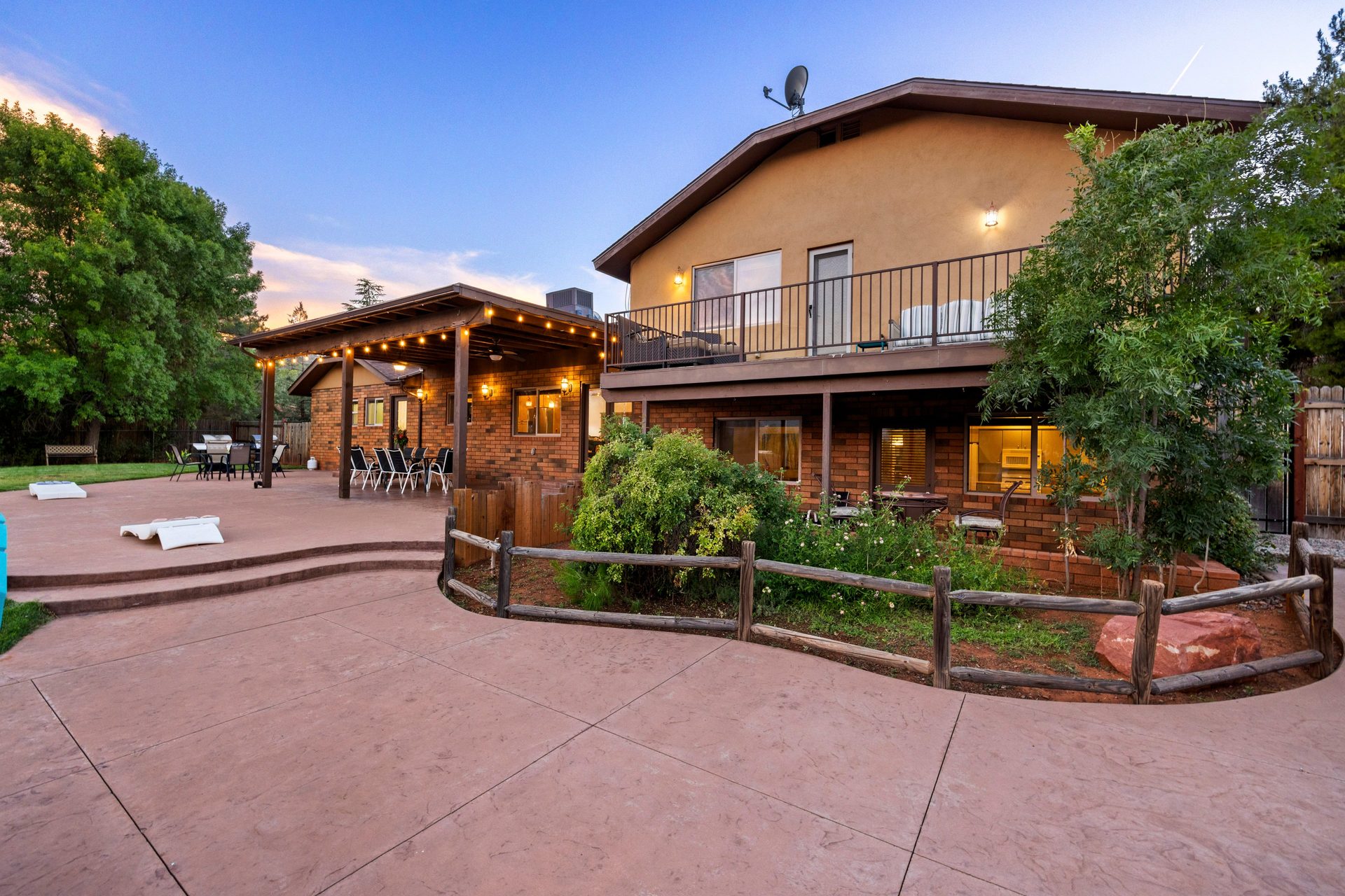 Spacious back patio with covered pergola, string lights, and cornhole at dusk
